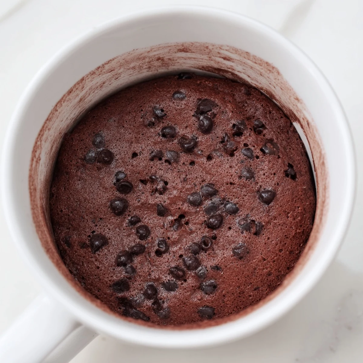 A close-up of a single-serving, rich chocolate microwaved mug cake, still steaming in its mug.