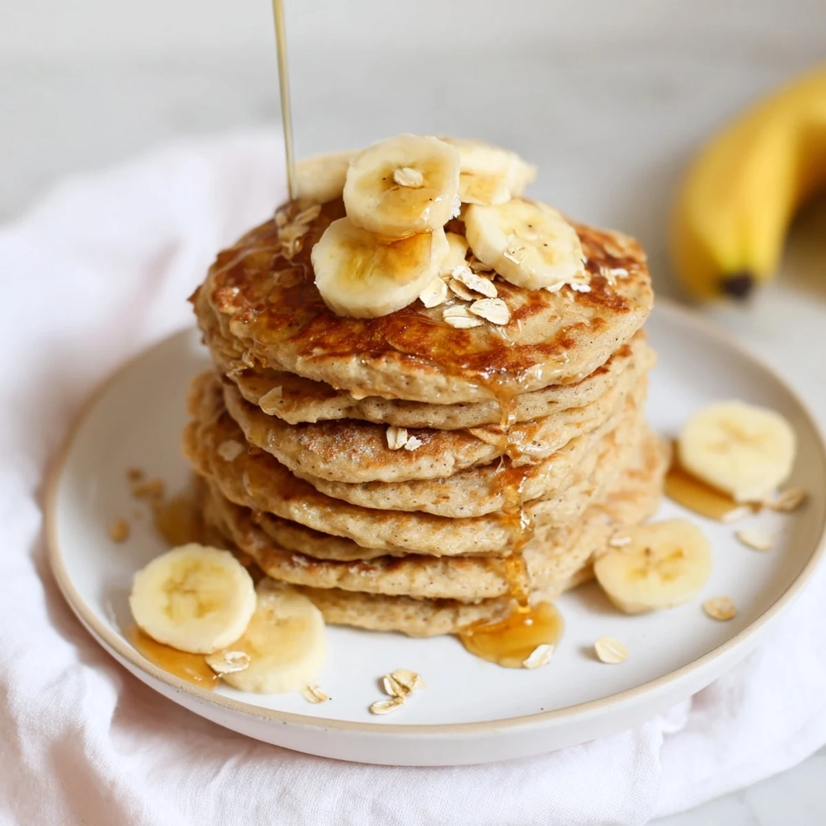 Golden-brown banana oat pancakes stacked high, ready to be drizzled with sweet maple syrup.