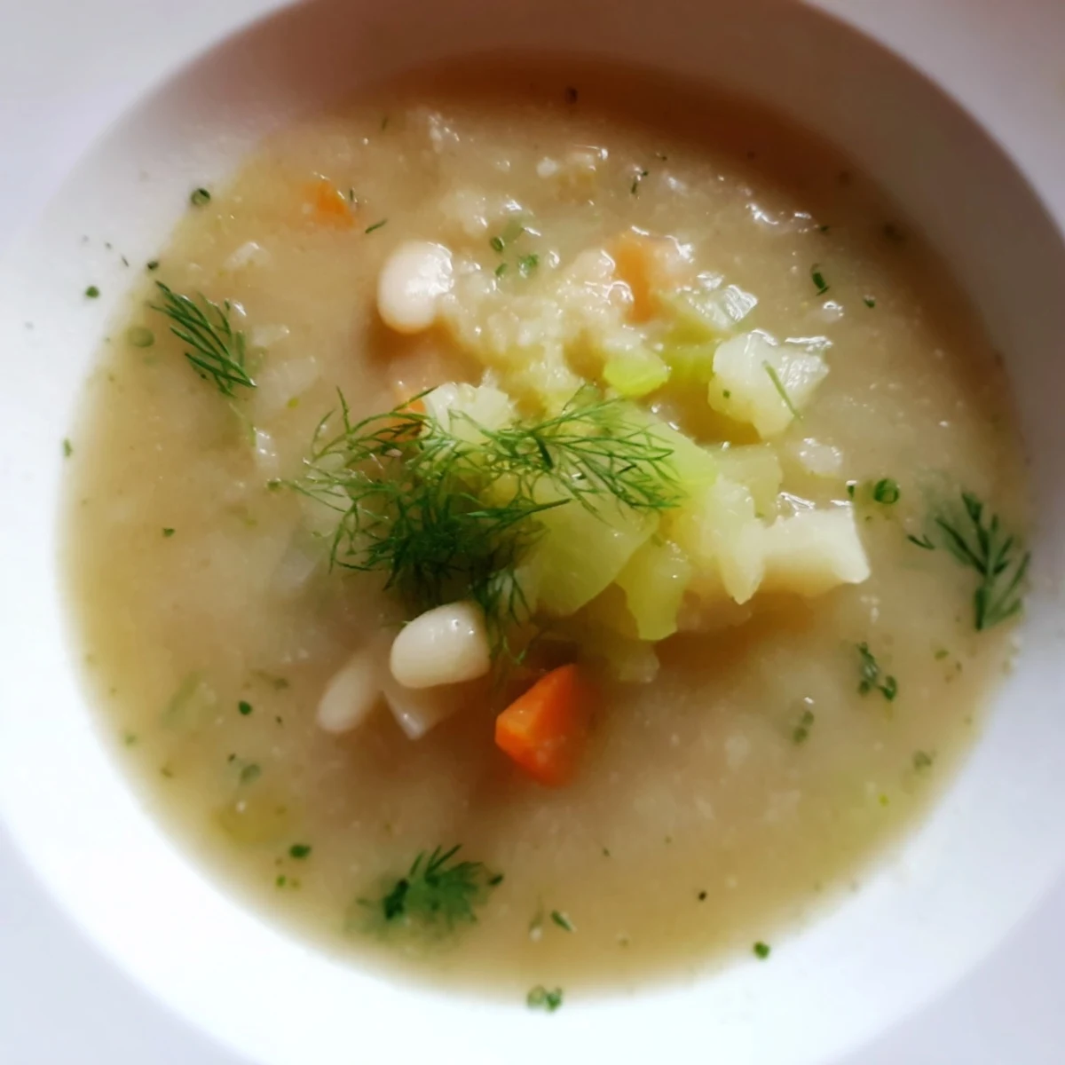 A close-up of creamy, flavorful Simple White Bean and Fennel Soup in a warm bowl, drizzled with olive oil.