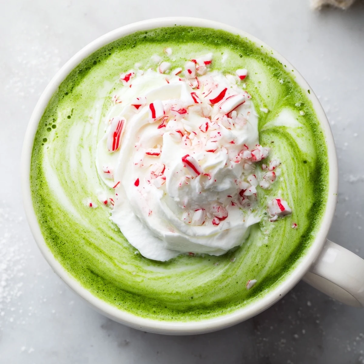 Steaming Cozy Peppermint Matcha Christmas Latte topped with whipped cream and crushed peppermint candies.