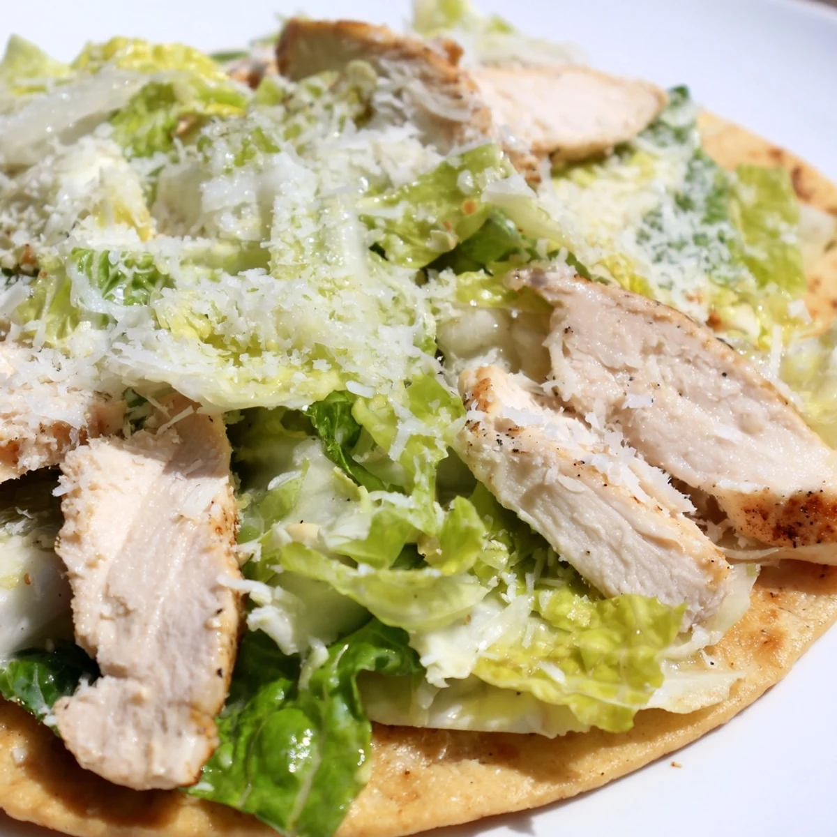 Sliced, tender grilled chicken rests on a warm flatbread base with crisp romaine lettuce, tangy Caesar, and parmesan for a classic Italian-American flavor.