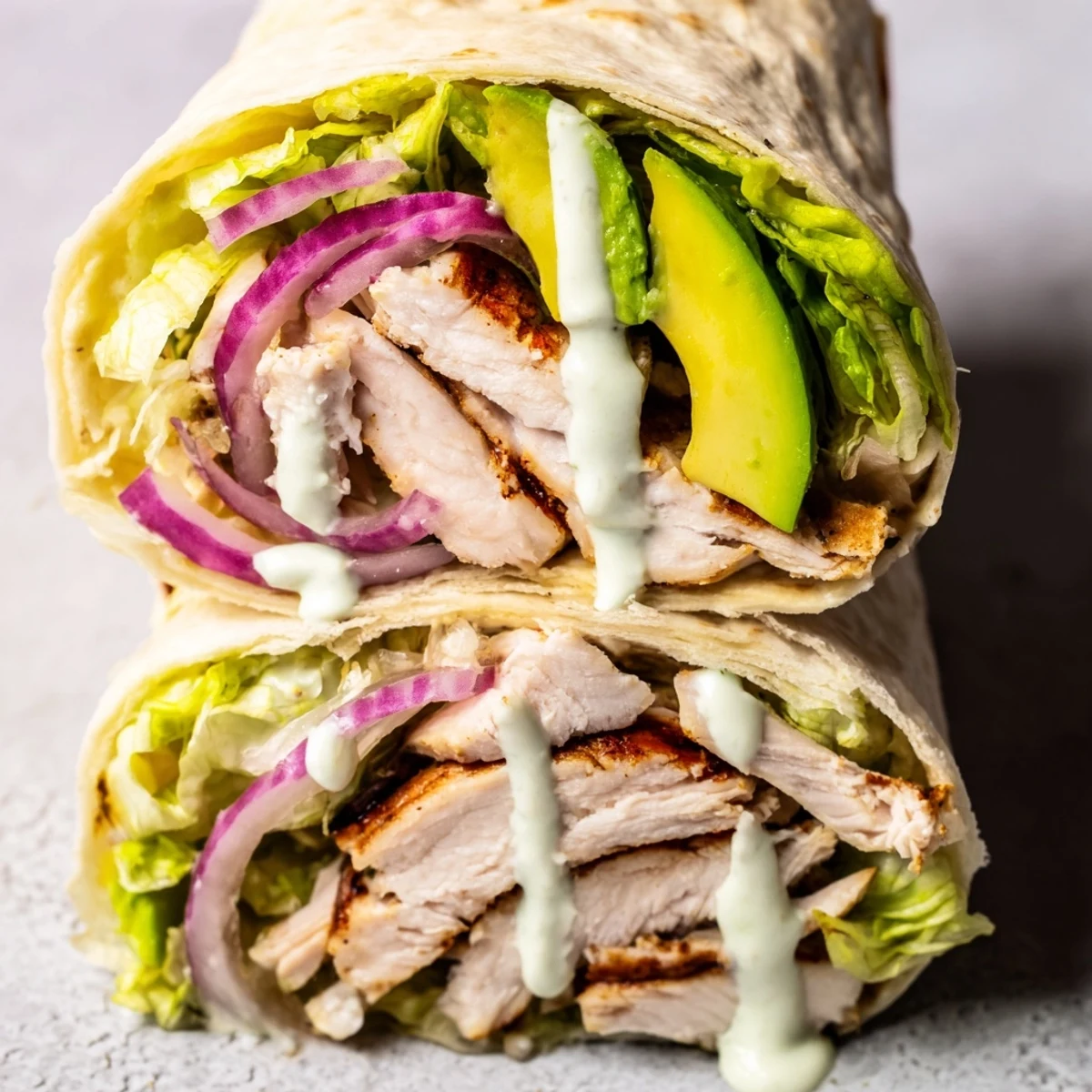 Fresh cilantro, red onion, and lime-spiked Greek yogurt drizzle over smoky chipotle chicken wraps served on a wooden board.