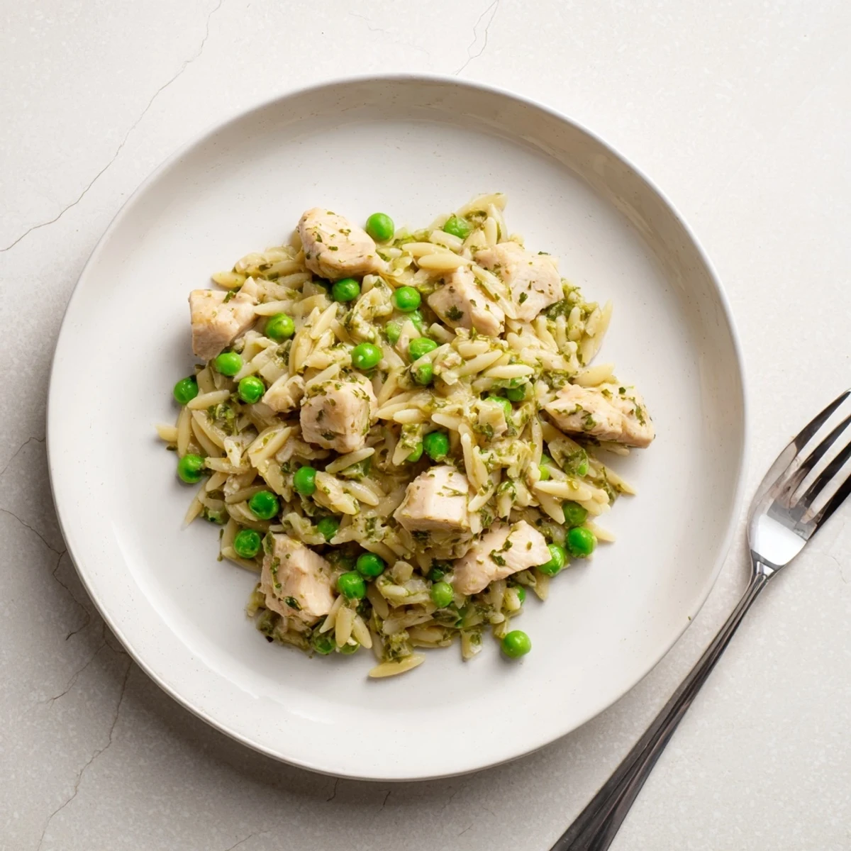 Tender chicken thighs and orzo pasta simmer in a zesty lemon sauce with bright green peas and fresh herbs, served steaming in the skillet.  
