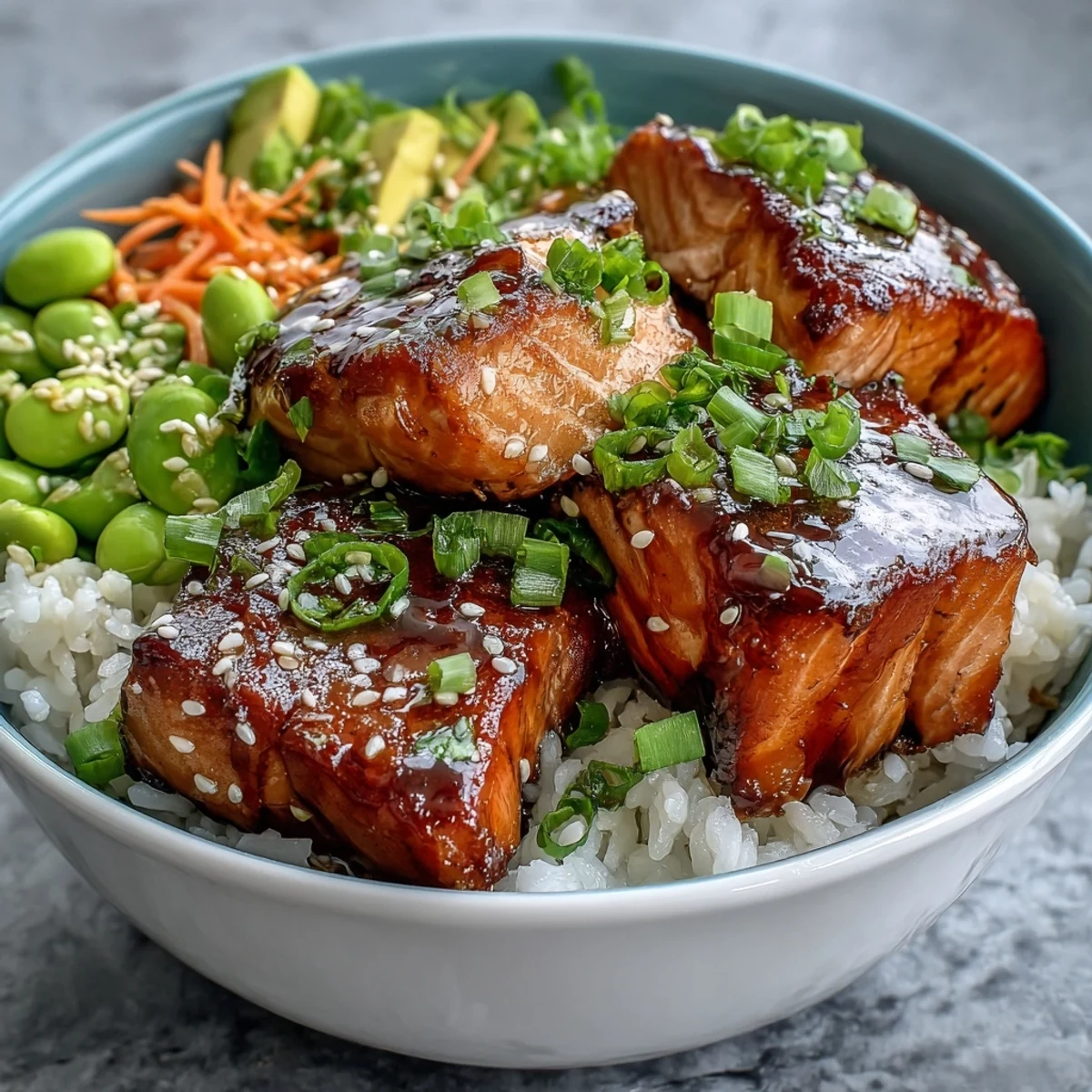 A close-up of the Baked Salmon Rice Bowl shows crisp cucumbers, shredded carrots, and creamy avocado slices beside savory salmon.