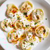 Steaming plate of Turkish cheesy manti, with a vibrant red spiced butter sauce, perfect meal.