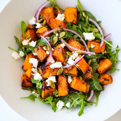 Golden roasted sweet potato salad with peppery arugula and creamy feta crumbles, topped with a bright honey-lime dressing.