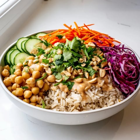 A vibrant Peanut Chickpea Rice Bowl with fluffy brown rice, chickpeas, crunchy peanuts, and colorful shredded vegetables, drizzled with creamy peanut dressing.  