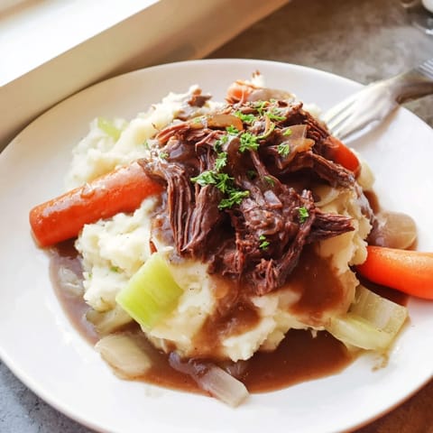 Tender Slow Cooker Pot Roast sits atop buttery mashed potatoes, drizzled in savory juices.  