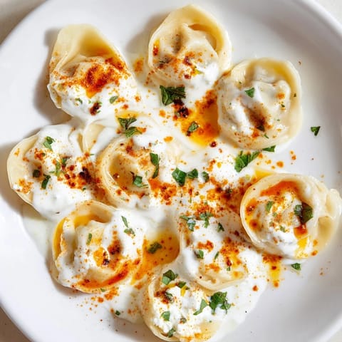 Steaming plate of Turkish cheesy manti, with a vibrant red spiced butter sauce, perfect meal.
