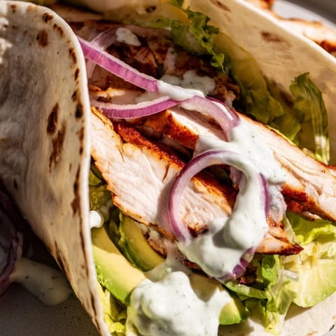 A close-up shows juicy marinated chicken nestled inside a soft wrap with bright lettuce and diced tomatoes.