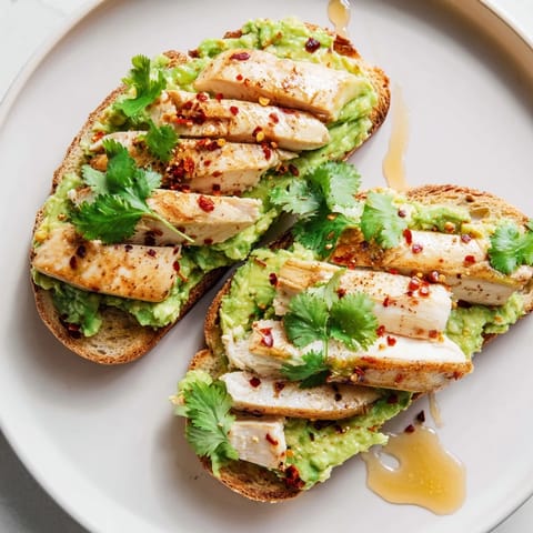 A close-up of Smashed Avocado Chicken Toast, garnished with fresh herbs and a drizzle of honey on rustic bread.  