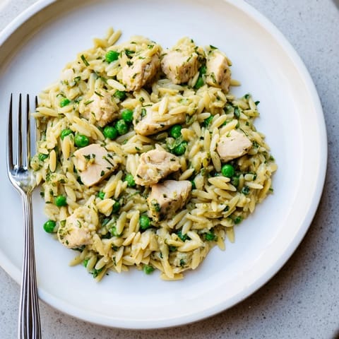 Golden chicken pieces and al dente orzo pasta are studded with sweet green peas in a single skillet, garnished with chopped parsley and dill.  