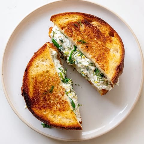 A close-up view of a warm whipped feta spring grilled cheese sandwich on a cutting board, revealing melted layers inside.