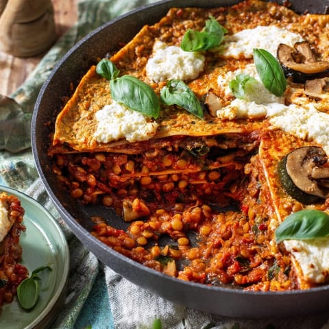 Layered slice of One-Pan Smoky Veggie Lentil Lasagne on a white plate, revealing hearty red lentils, mushrooms, and zucchini.  