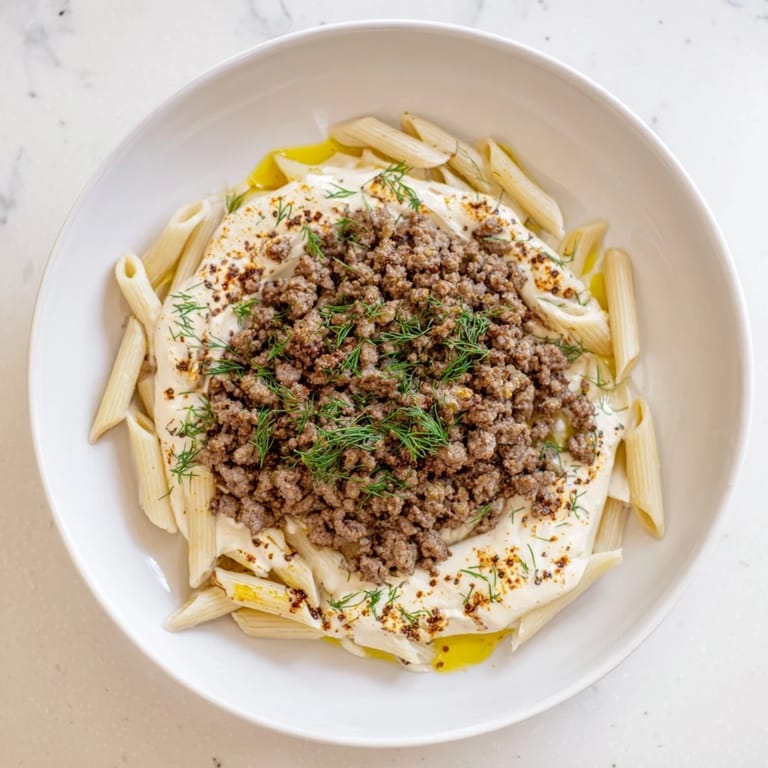 A close up shows the vibrant Turkish Pasta with Ground Turkey, perfectly garnished and ready to eat with a swirl of butter.