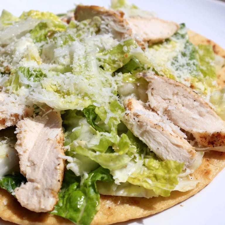 Sliced, tender grilled chicken rests on a warm flatbread base with crisp romaine lettuce, tangy Caesar, and parmesan for a classic Italian-American flavor.